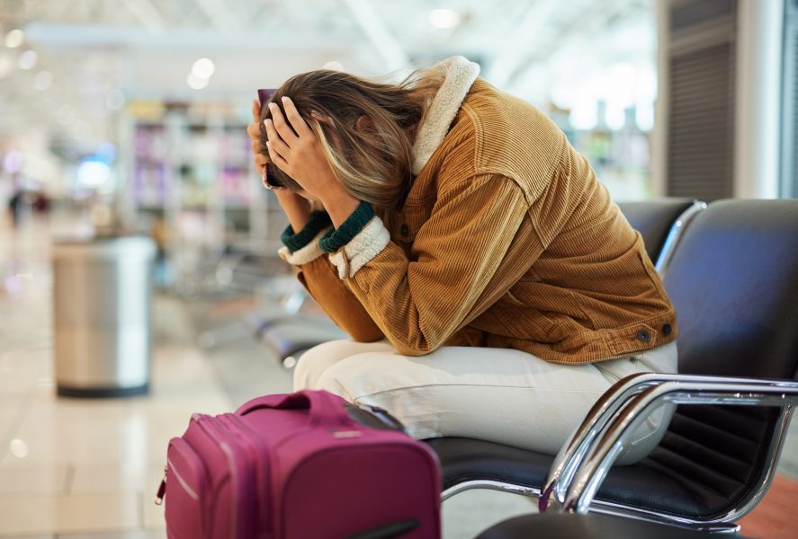 Upset woman, airport and flight delay sitting on bench in travel restrictions or plane cancelation with luggage. Angry, sad or disappointed female in frustration for missing boarding schedule time.