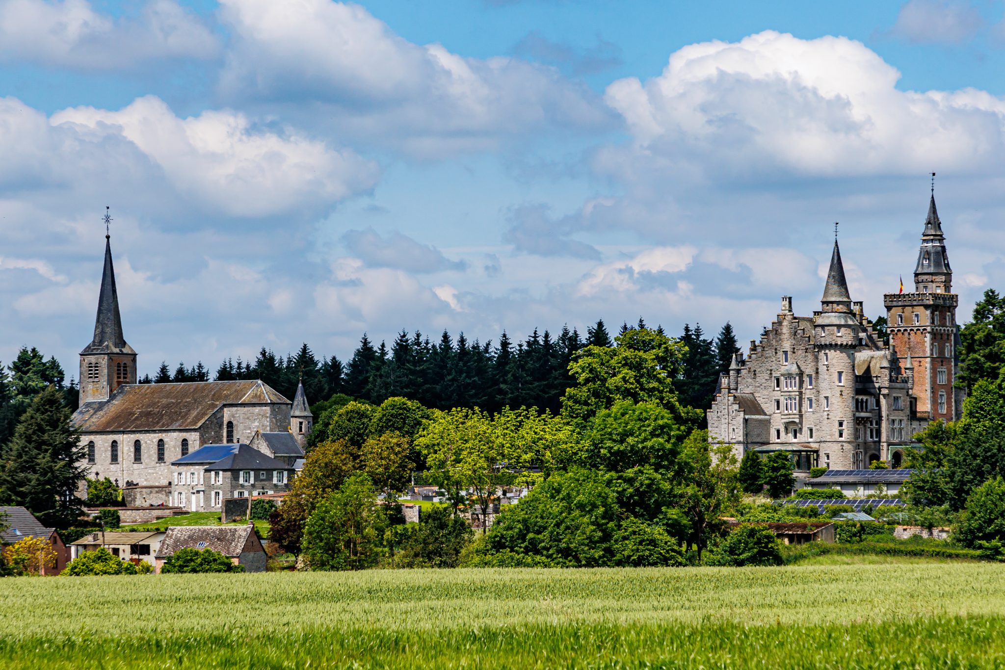 Leignon Castle and Collegiate Church of Our Lady of Assumption or Church of Saint Nicholas, agricultural field, leafy trees against blue sky sunny summer day in Ciney, province of Namur, Belgium